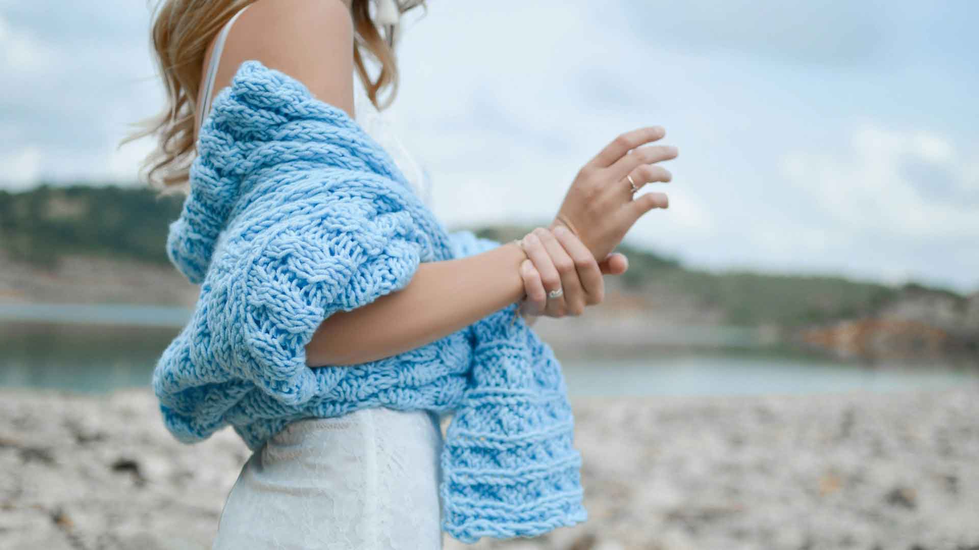 Woman on beach with stylish blue spring sweater.